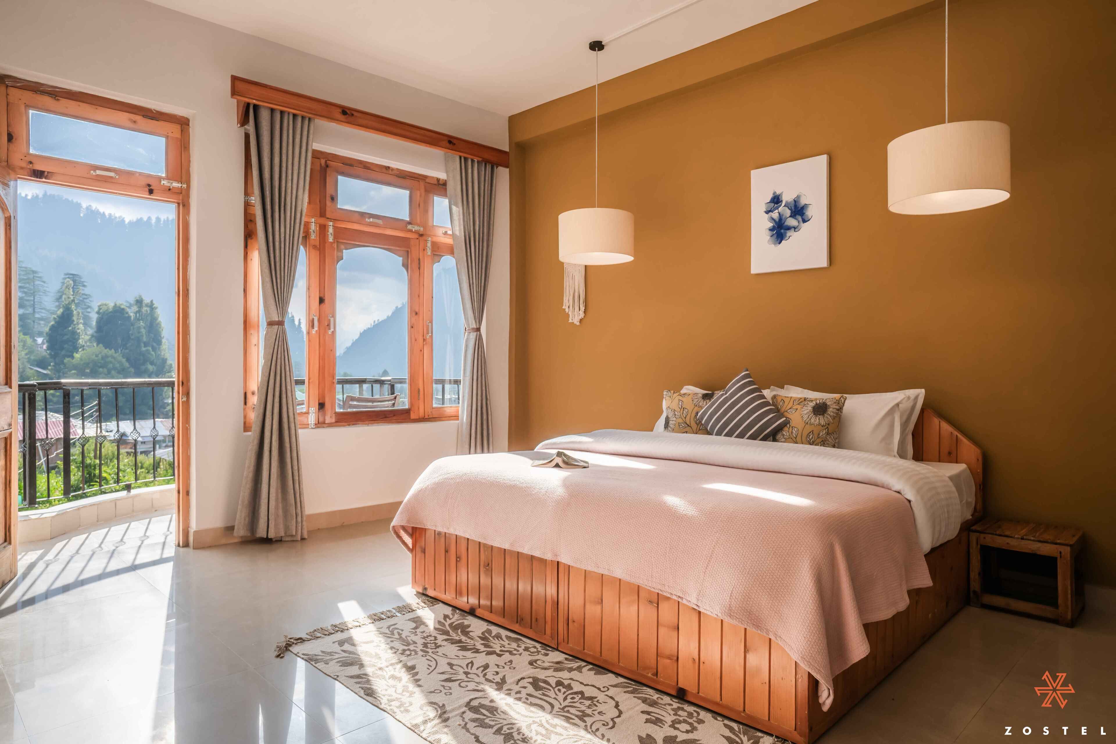 Een slaapkamer met een houten bed, twee hanglampen, een raam met gordijnen en uitzicht op bergen.