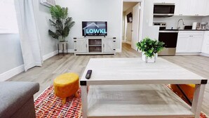 A modern living room with a TV, a dining table, and a kitchen area. - Spacious 1-Bedroom in Coral Ridge with King Bed, Sofa Bed & Pool Access (fort lauderdale)
