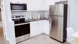A modern kitchen with white cabinets, stainless steel appliances, and a wooden floor. - Spacious 1-Bedroom in Coral Ridge with King Bed, Sofa Bed & Pool Access (fort lauderdale)