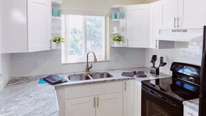 Una cocina moderna con armarios blancos, encimera de granito, horno negro y pileta de acero inoxidable.