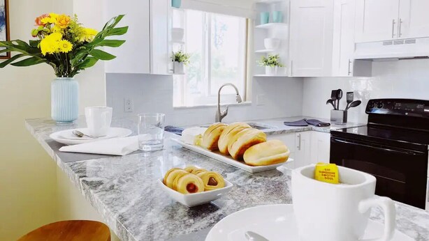 Una cocina moderna con armarios blancos, encimera de mármol y ventana que proporciona luz natural.