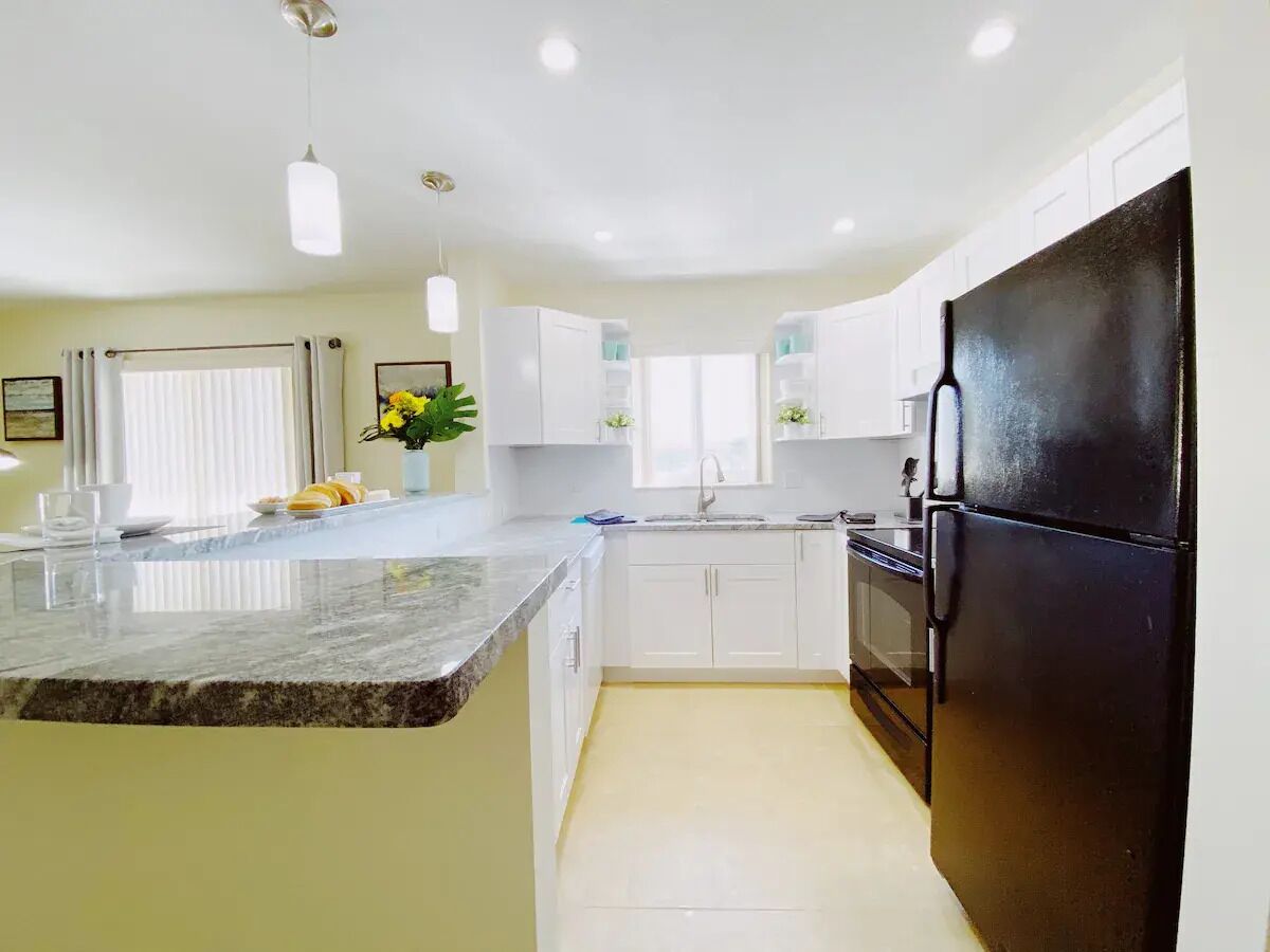 A modern kitchen with white cabinets, a black refrigerator, and a granite countertop.