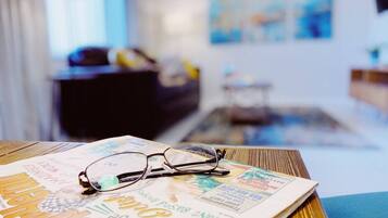 A pair of glasses on a magazine on a wooden table in a room with a blue wall and a window.