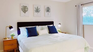 Une chambre à coucher comprenant un lit, des tables de chevet, une fenêtre avec des rideaux et des œuvres d’art murales.