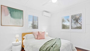 Ein Schlafzimmer mit einem Bett, zwei Nachttischen, einer Wand-Klimaanlage und einem Fenster mit Metallgitter.
