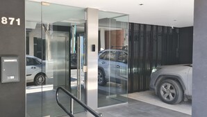 Entrada de un edificio moderno con puerta de cristal, placa metálica con un número y un coche estacionado en el interior.