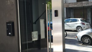 Entrada moderna de un edificio con puerta de vidrio, el número '3871' visible y un coche estacionado afuera.