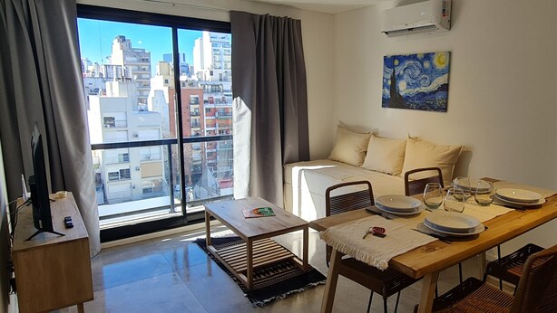 Un apartamento moderno con comedor, sofá y un amplio ventanal con cortinas.