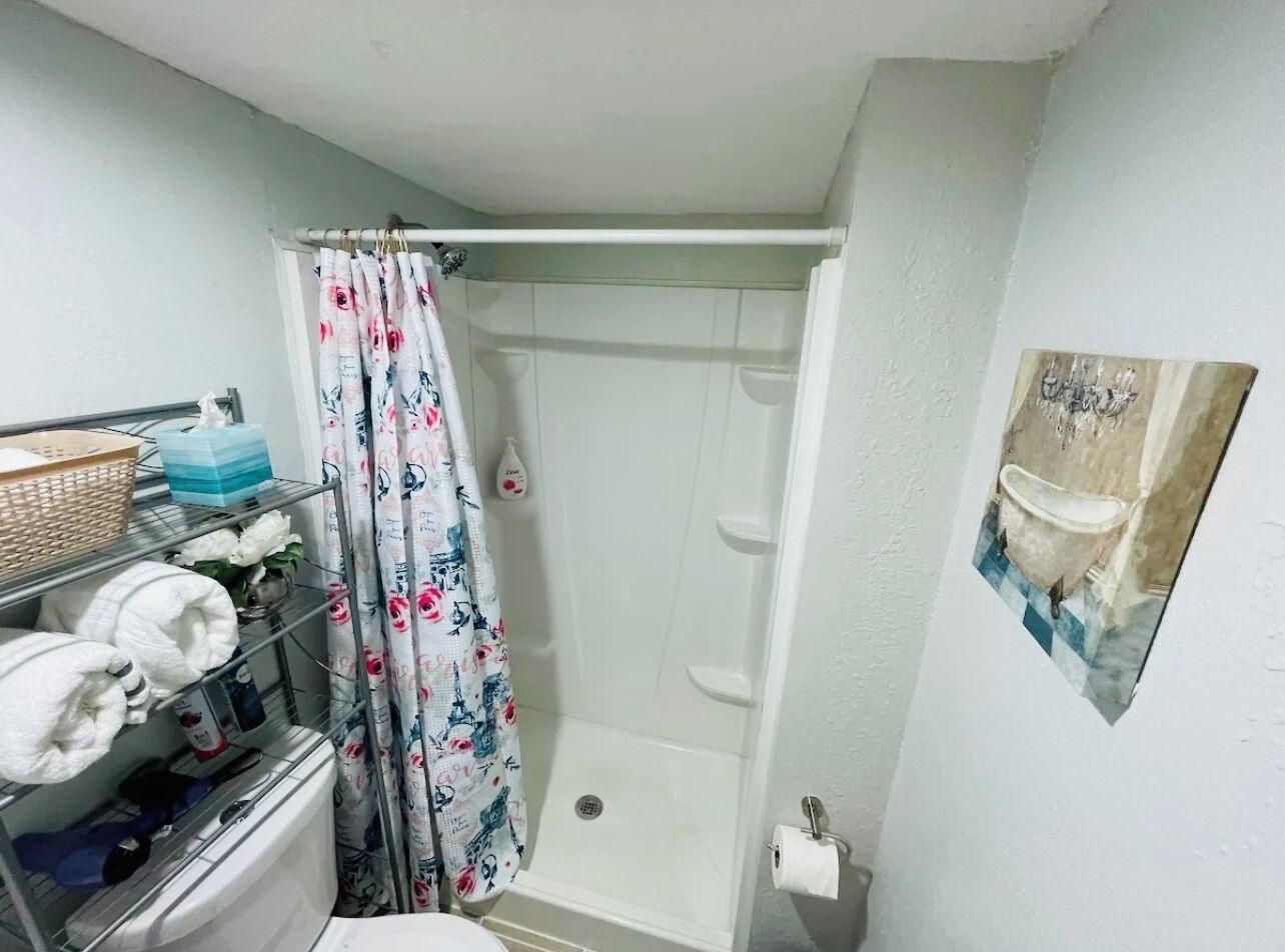 Un baño pequeño con ducha, inodoro y lavamanos. Hay un estante con toallas y artículos de aseo.