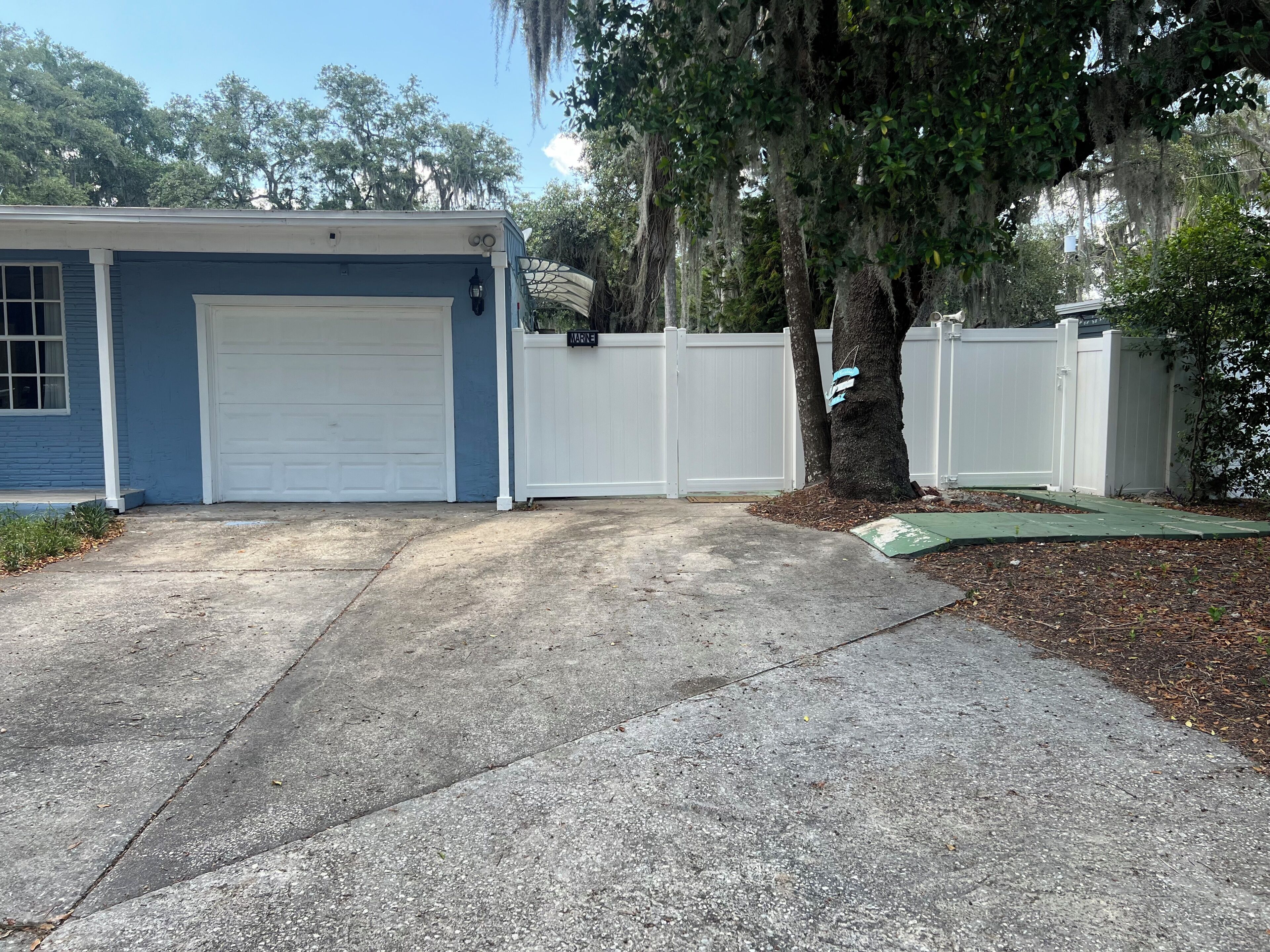 A residential garage with a white door, a blue exterior wall, and a white fence.