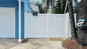 Una puerta de garaje, una valla blanca y un árbol con un letrero.