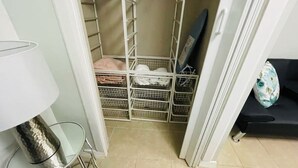 Una habitación con un estante metálico, una mesa de vidrio y un sofá negro.