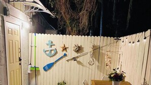 Un patio al aire libre con una mesa y sillas de madera, una planta pequeña en maceta y varios objetos decorativos como una pala azul, estrellas de mar y una cuerda.