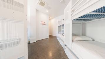 A dormitory room with bunk beds, a white wall with a red dot pattern, and a ceiling vent.