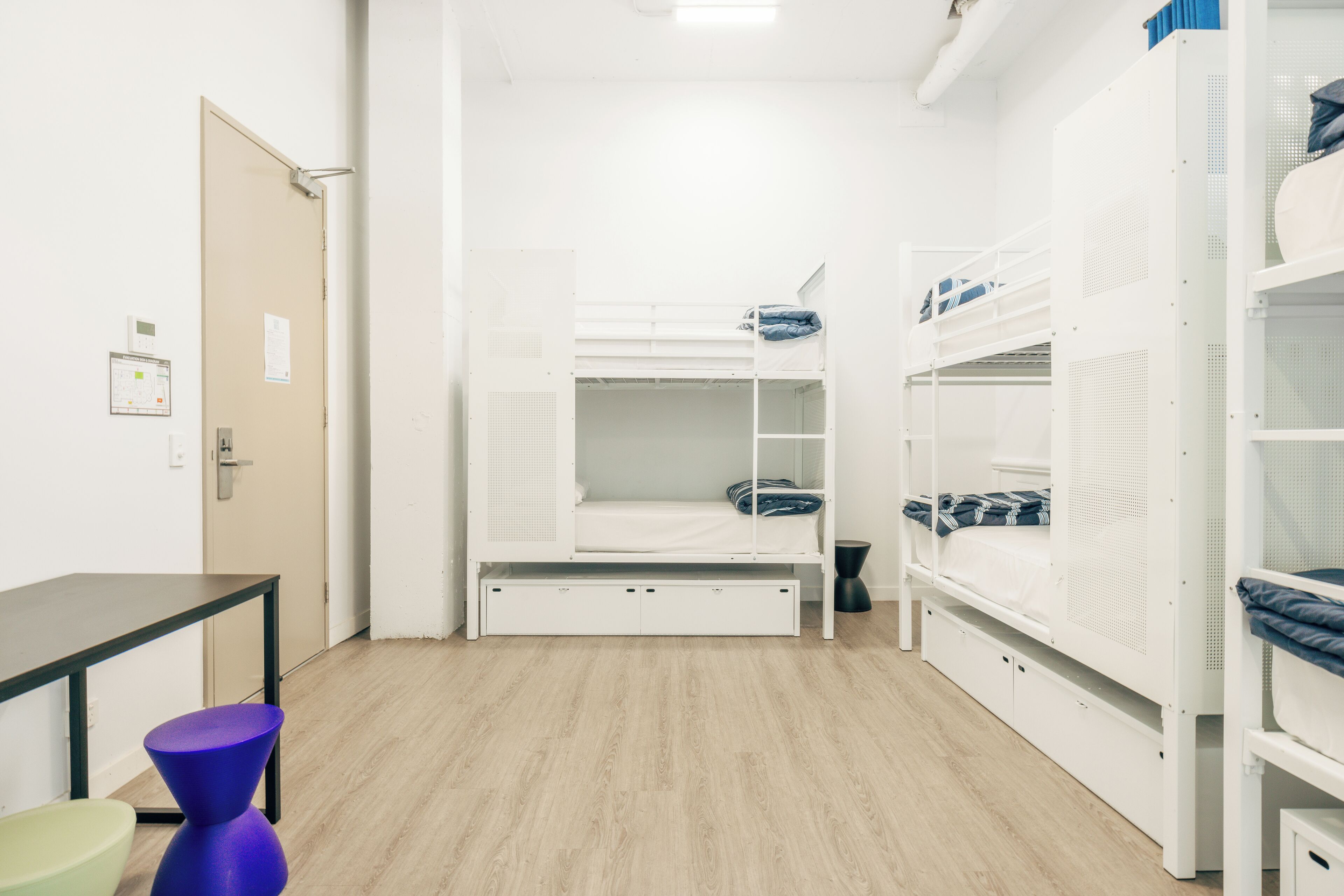 A dormitory room with bunk beds, a desk, and a chair.