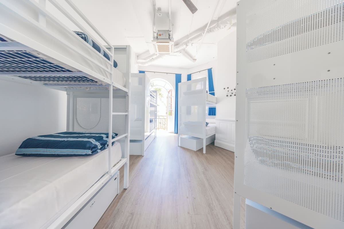 A narrow hallway with bunk beds on one side and a white partition with ventilation on the other.