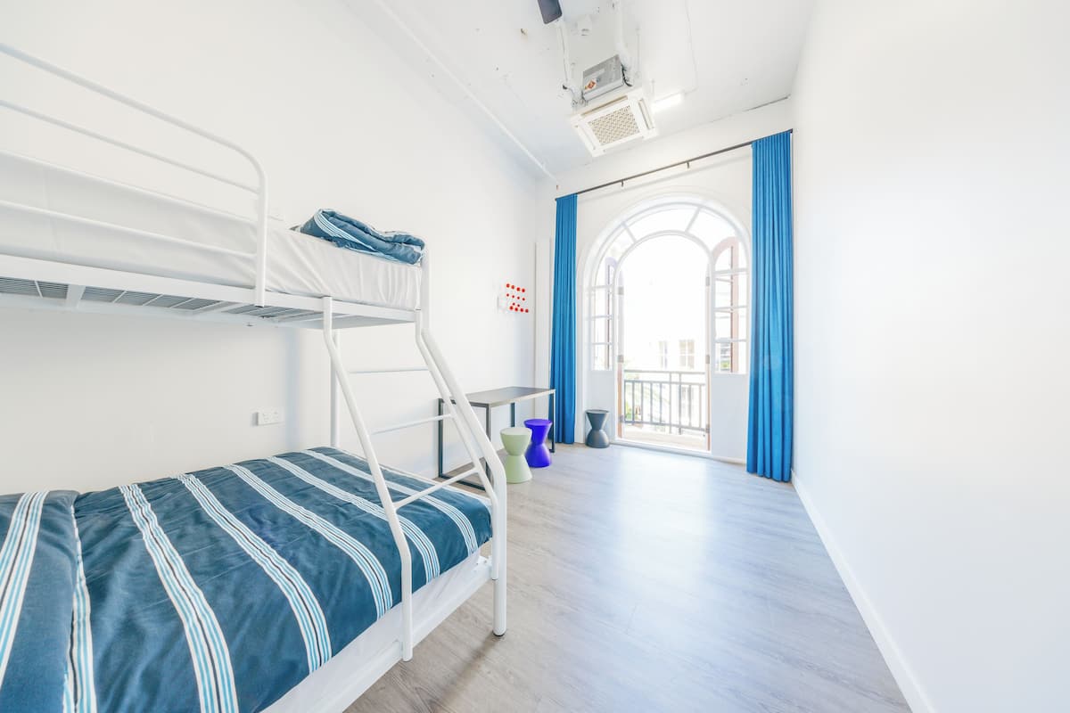 A bunk bed room with a window, a small table, and a blue curtain.