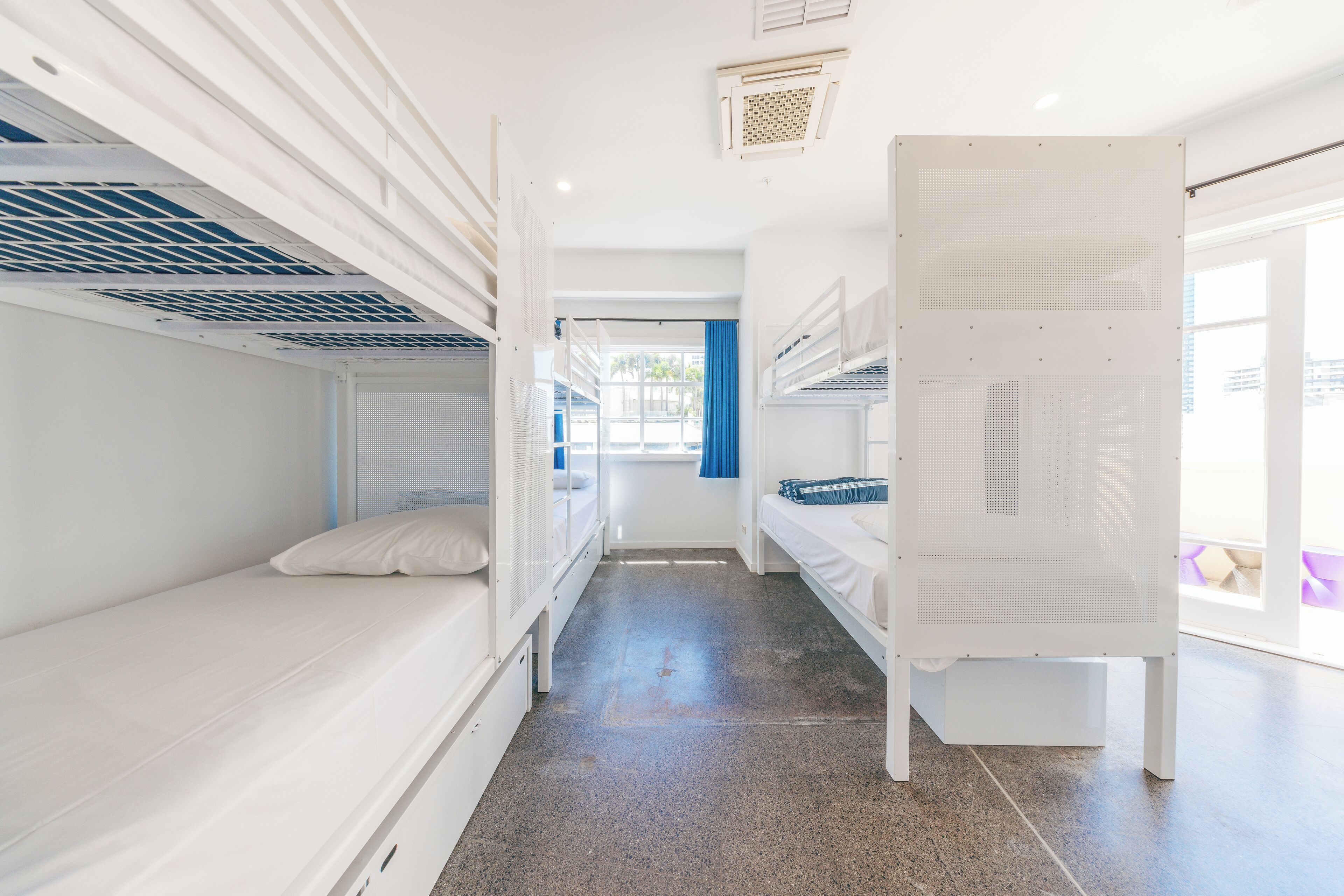 A bunk room with two bunk beds, a window with blue curtains, and a door leading to another room.