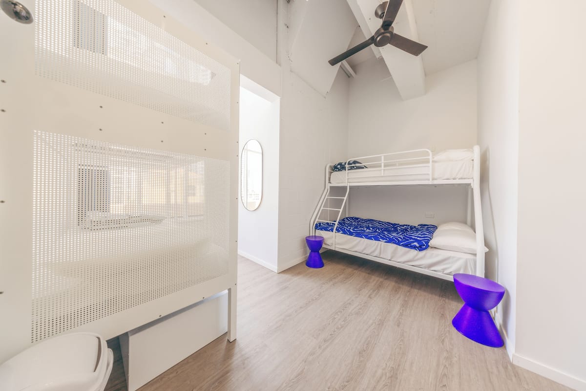 A room with a bunk bed, a white ceiling fan, a white radiator, and a purple stool.