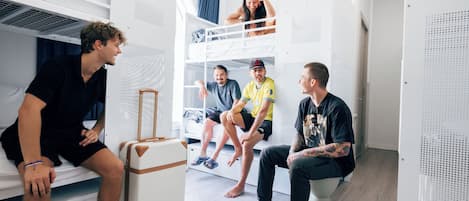 A bunk bed room with a suitcase and a person sitting on the lower bunk.