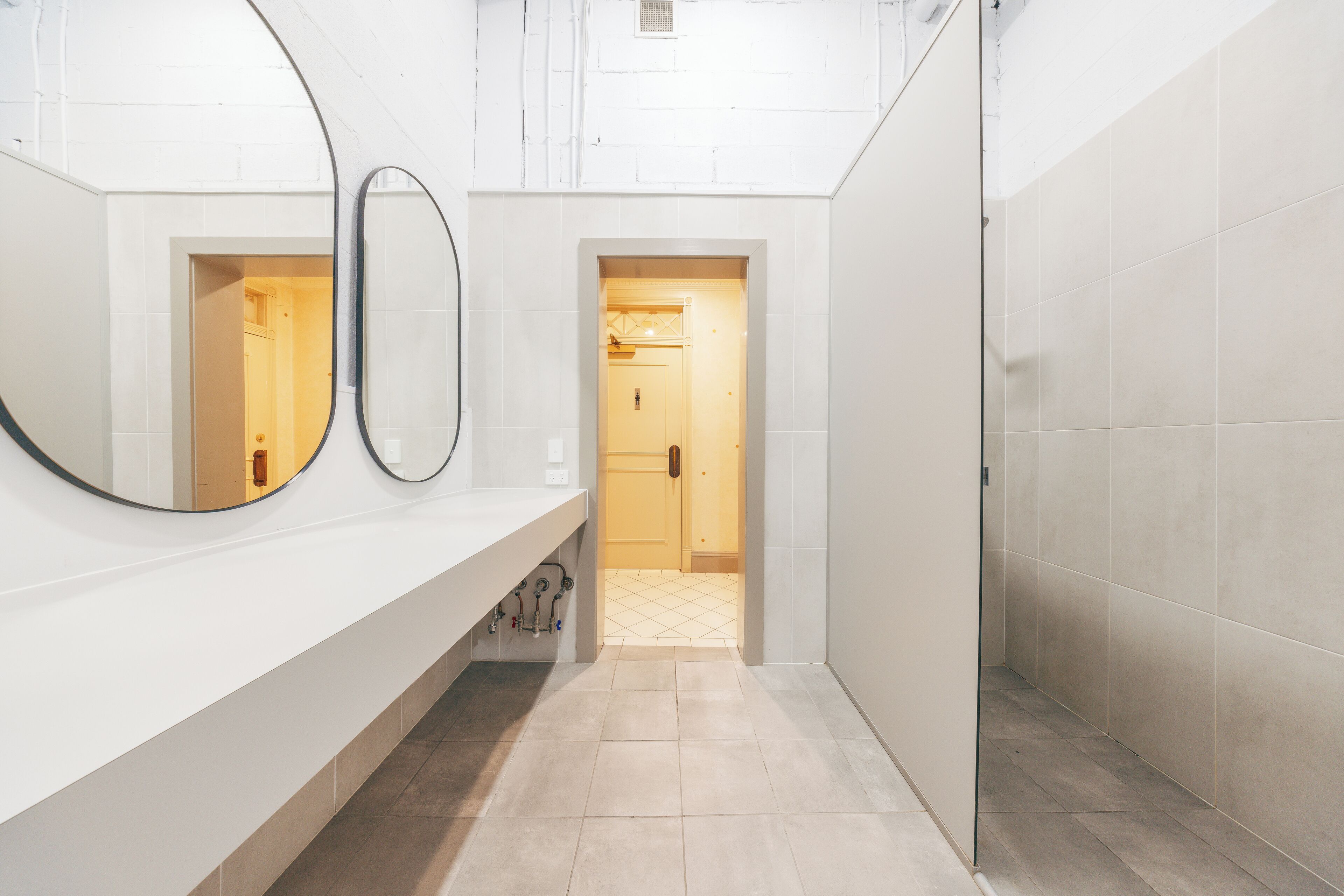 Une salle de bain moderne avec deux miroirs, un lavabo blanc et un sol carrelé.