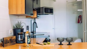 Une cuisine avec un plan de travail en bois, une machine à café, une bouteille, une planche à découper et deux bols en verre.