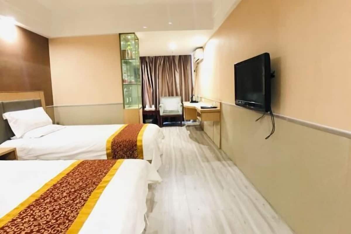 A hotel room with two beds, a desk, a chair, a television, and a glass display unit.