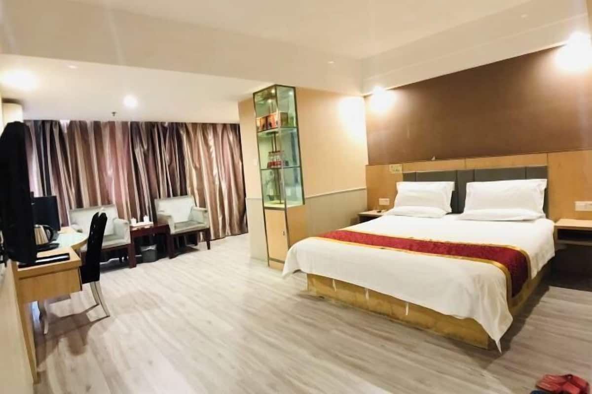 A hotel room with a bed, desk, chair, and a glass cabinet.