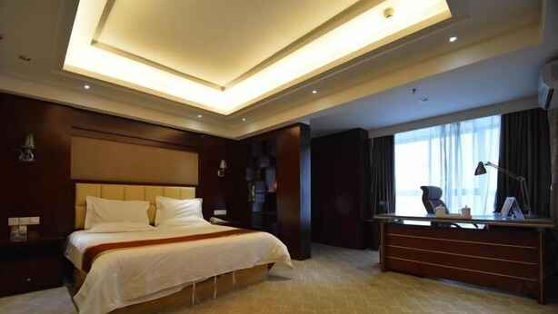 A hotel room with a large bed, a desk, and a view of the city through large windows. - Yiding Business Hotel (Yuxi Building Expo Center Subway Station Branch) (Zhengzhou)