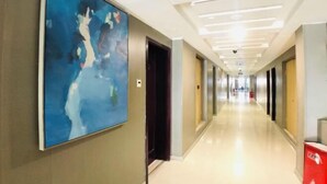 A hotel corridor with a large abstract painting on the left wall, a clean, well-lit hallway, and a red fire extinguisher on the right. - Yiding Business Hotel (Yuxi Building Expo Center Subway Station Branch) (Zhengzhou)