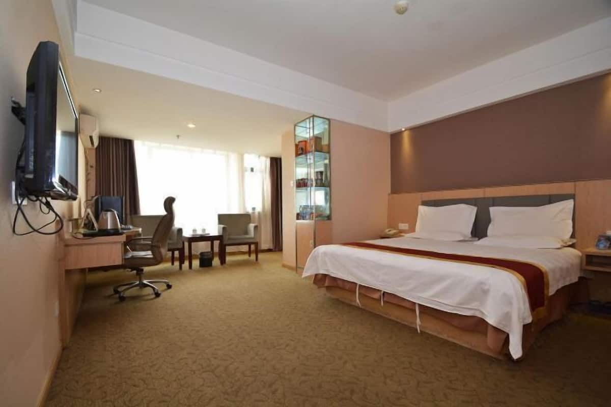 A hotel room with a bed, desk, chair, television, and a minibar.