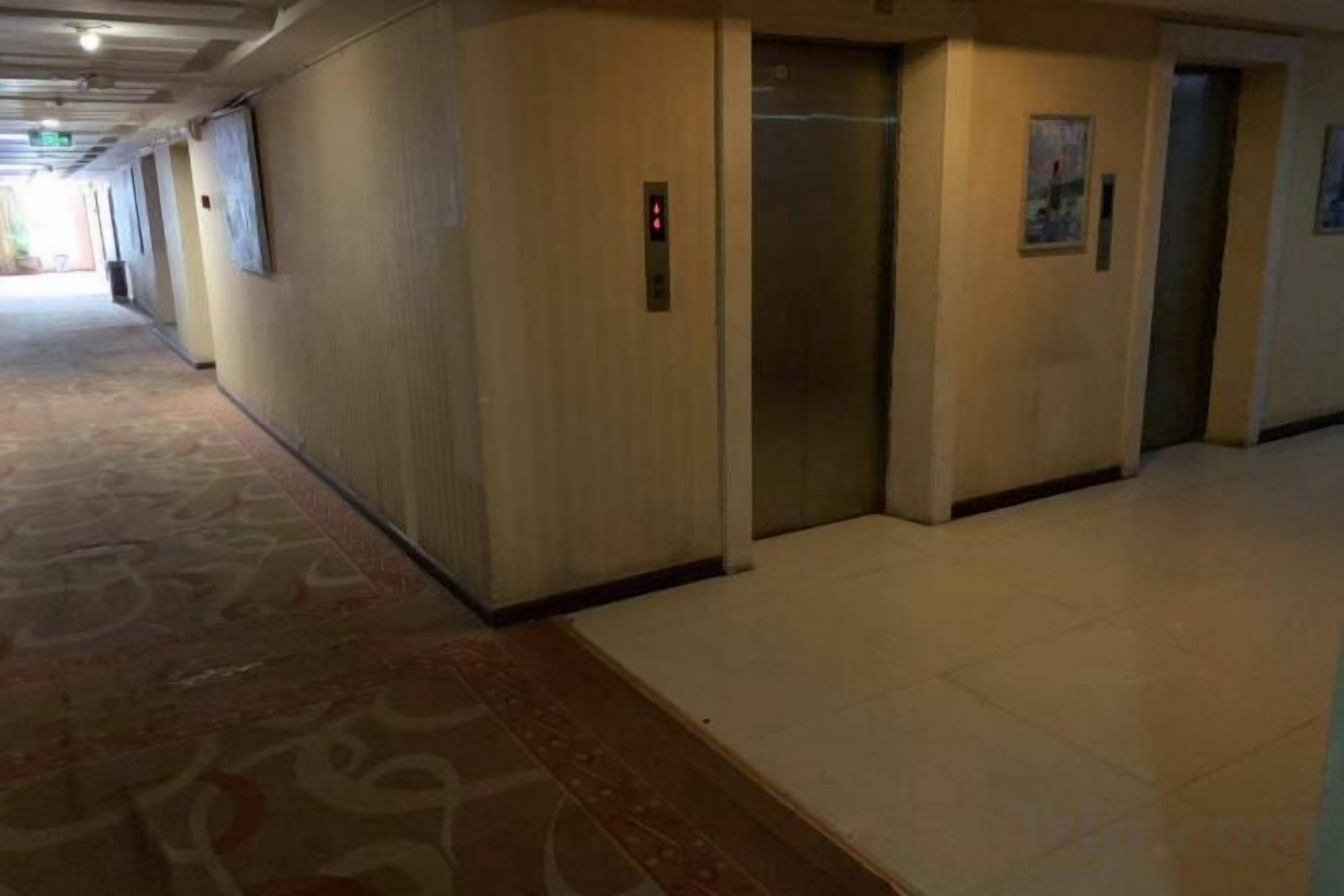 A hotel corridor with elevators, carpeted flooring, and a plain wall.