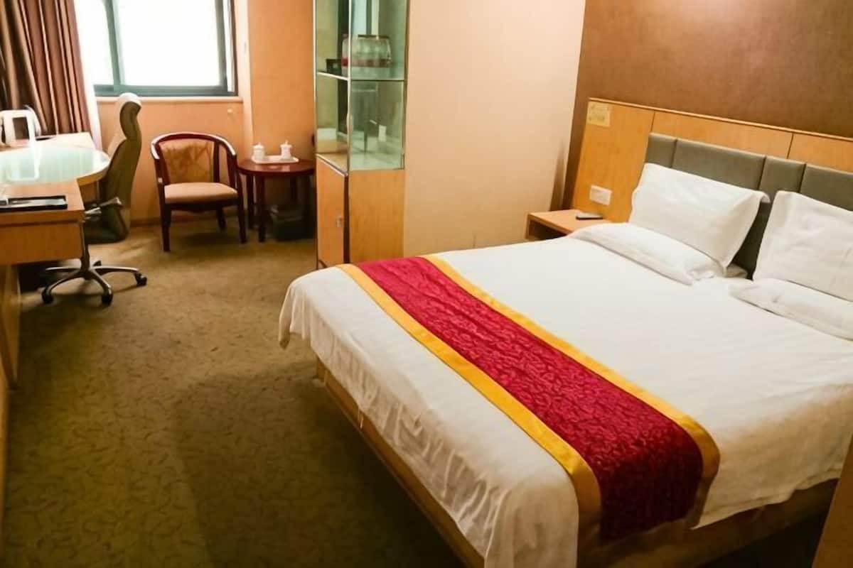 A hotel room with a bed, a desk, a chair, a small table, and a wardrobe.