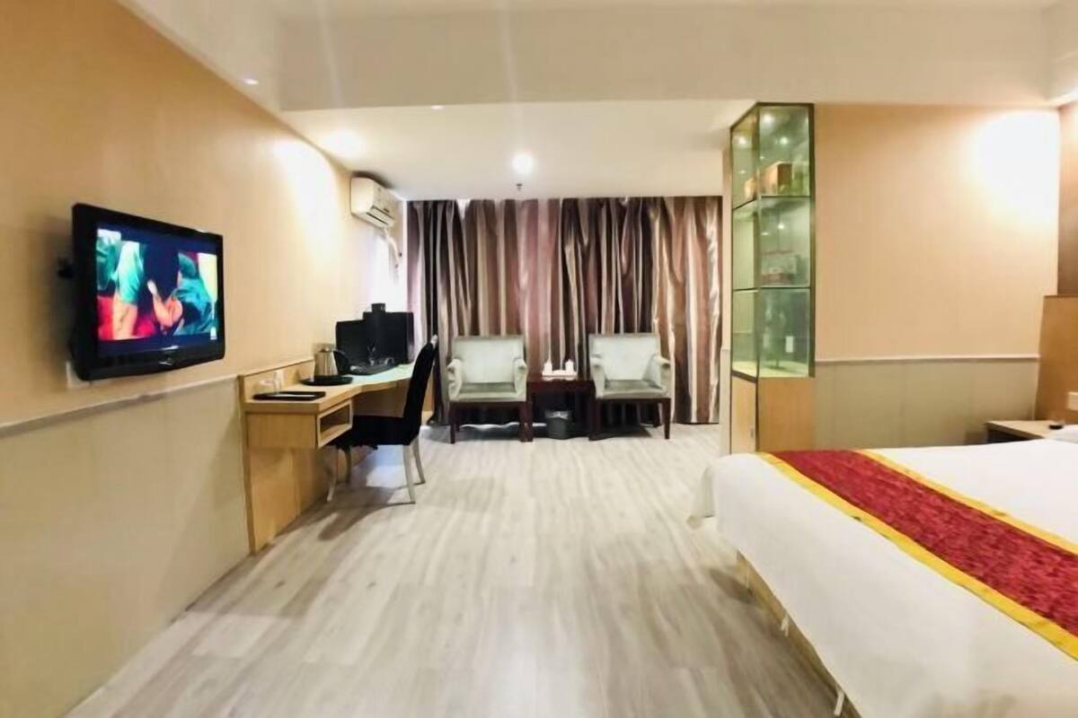 A hotel room with a bed, a desk with a chair, a television, and a glass cabinet.