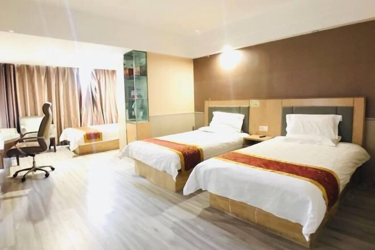 A hotel room with two beds, a desk, a chair, and a large window with curtains.