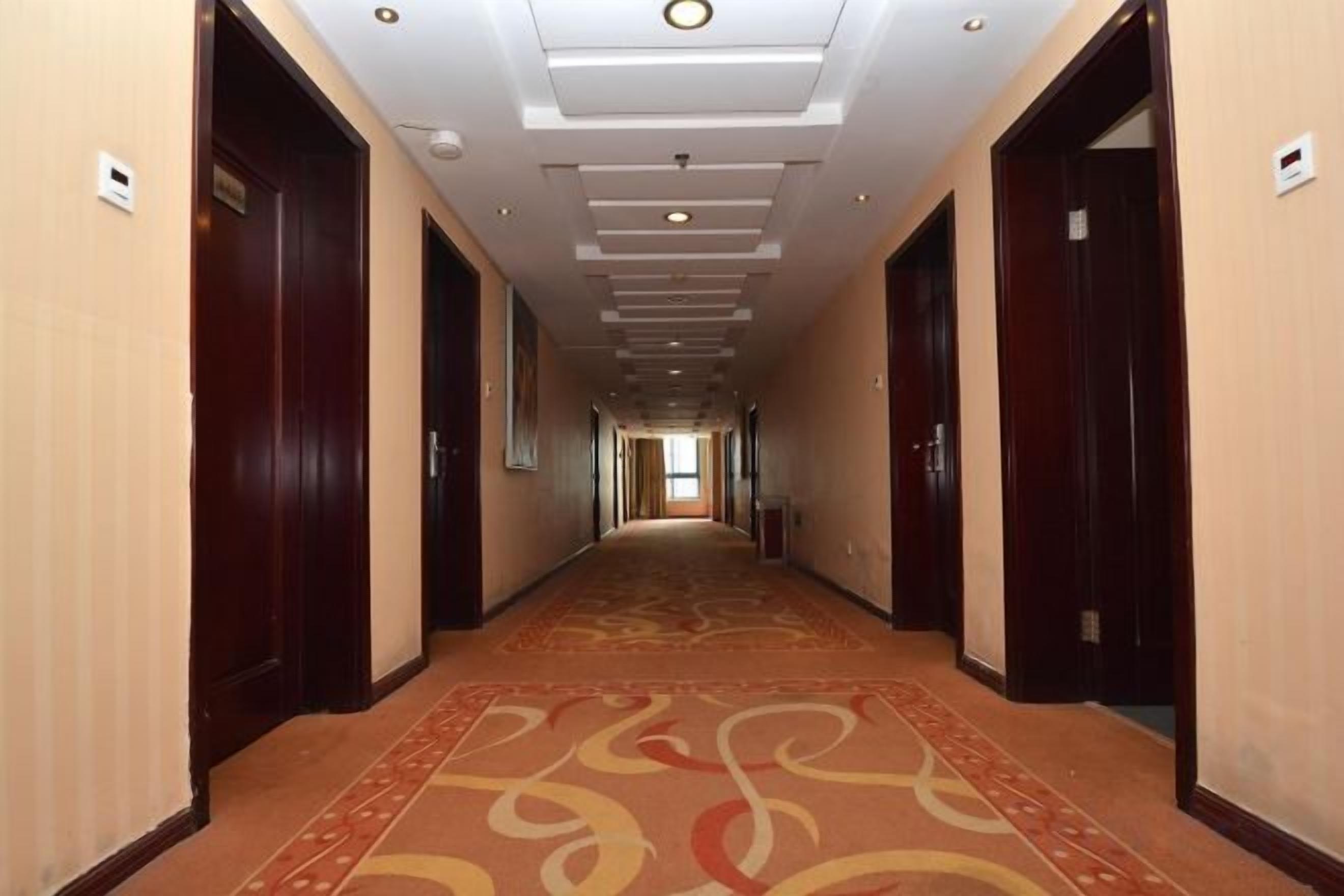 Ein Hotelkorridor mit Teppichböden, Holztüren und Einbuchtungslichtern.