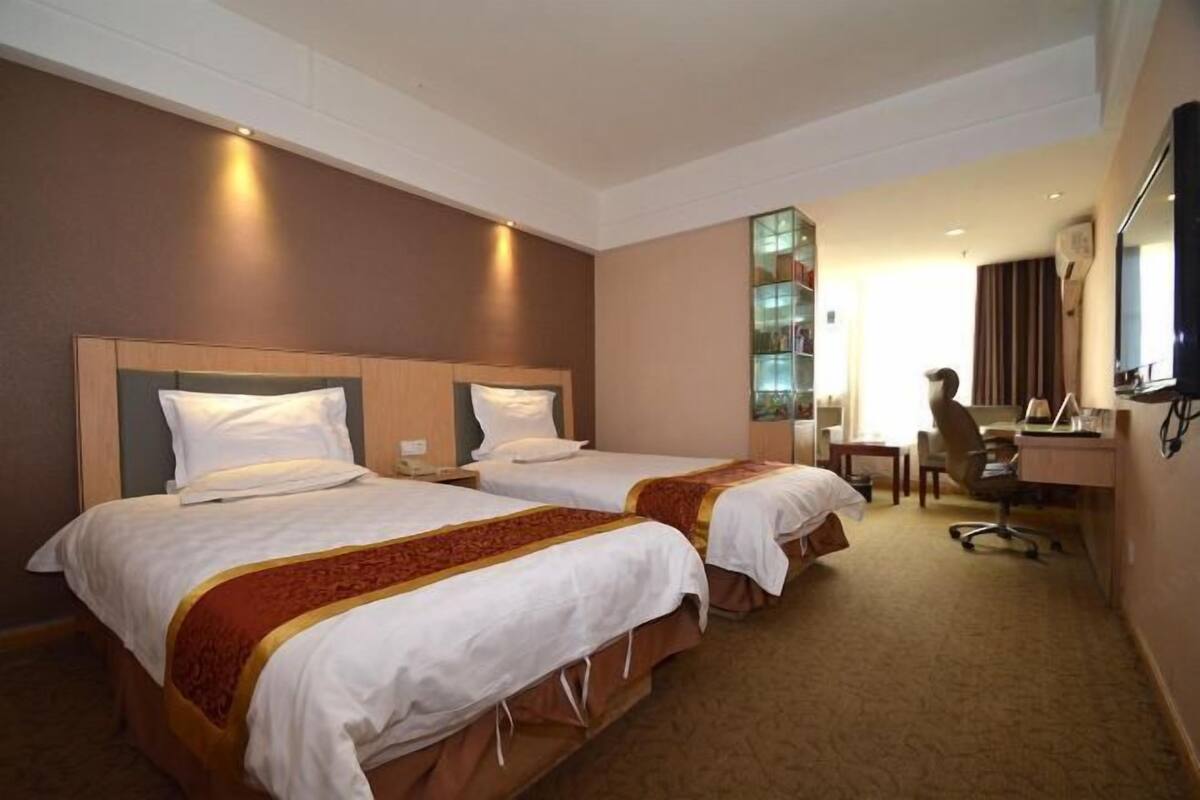 A hotel room with two beds, a desk, a chair, and a TV.