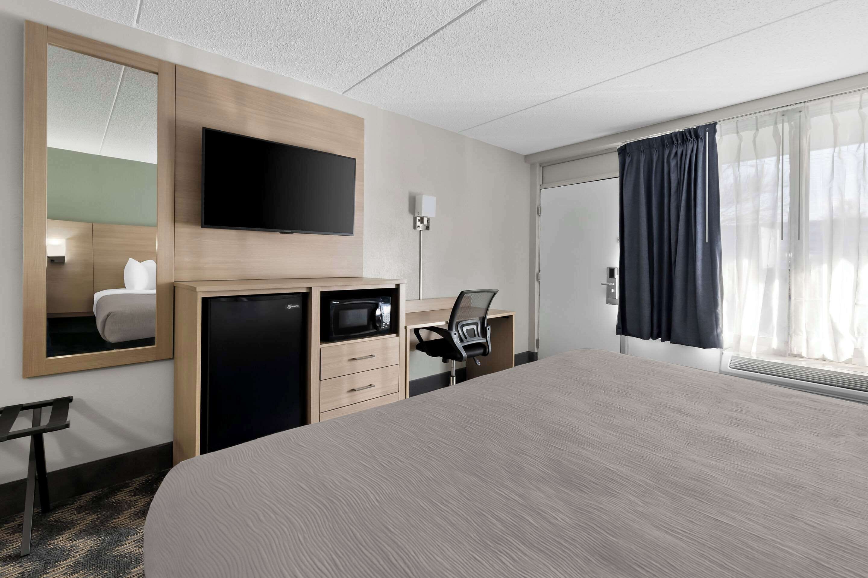 Een hotelkamer met een groot bed, een bureau met stoel, een televisie en een spiegel.