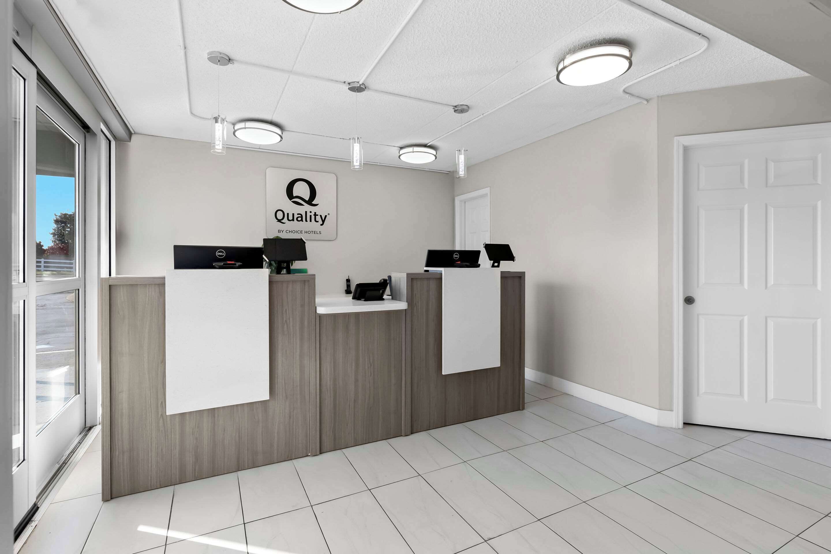 A reception area with a wooden reception desk, a sign reading "Quality by Choice Hotels," and a door to the right.