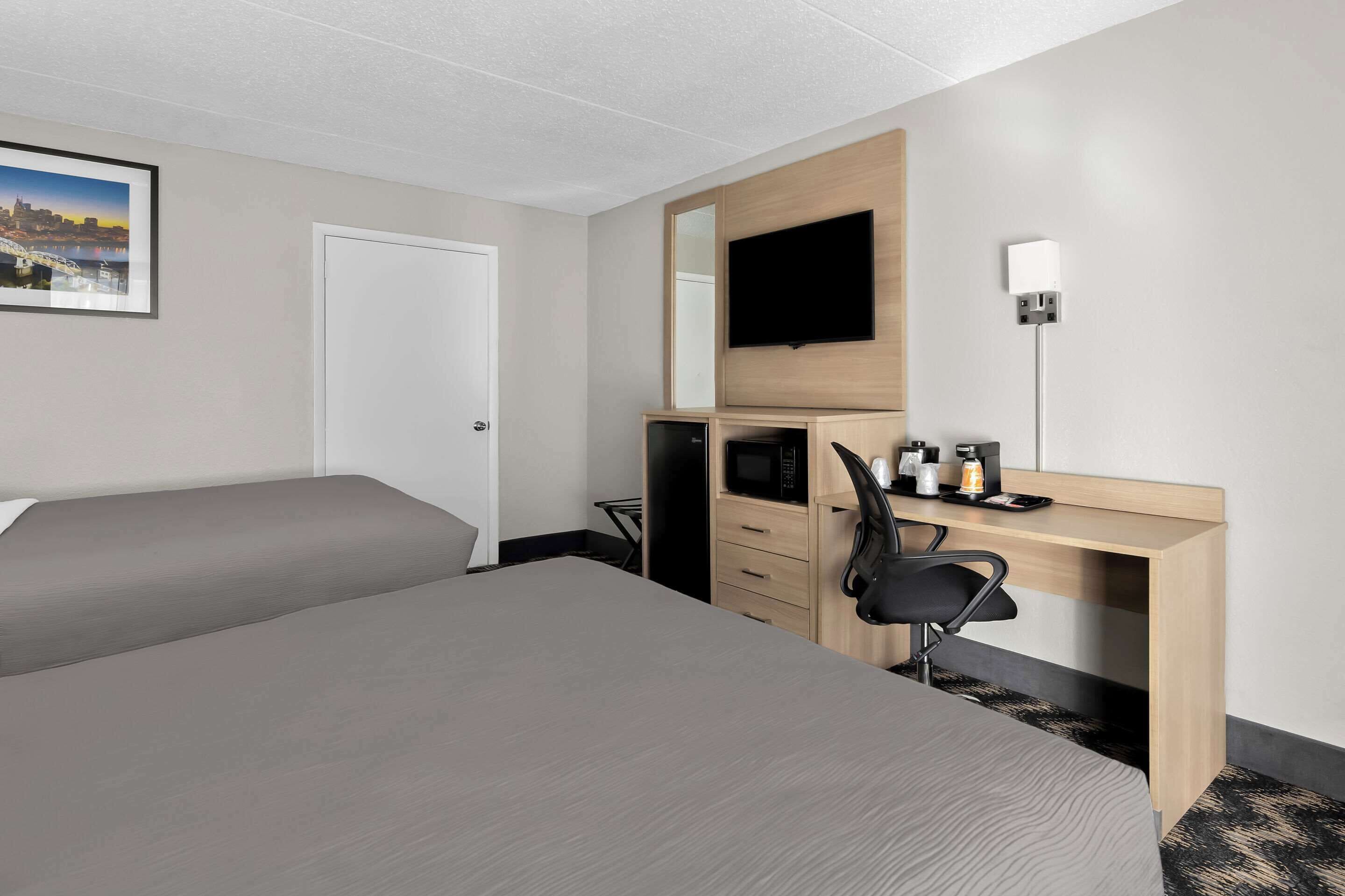 Ein Hotelzimmer mit einem großen Bett, einem Schreibtisch mit Computer, einer Mikrowelle und einem Flachbildfernseher.