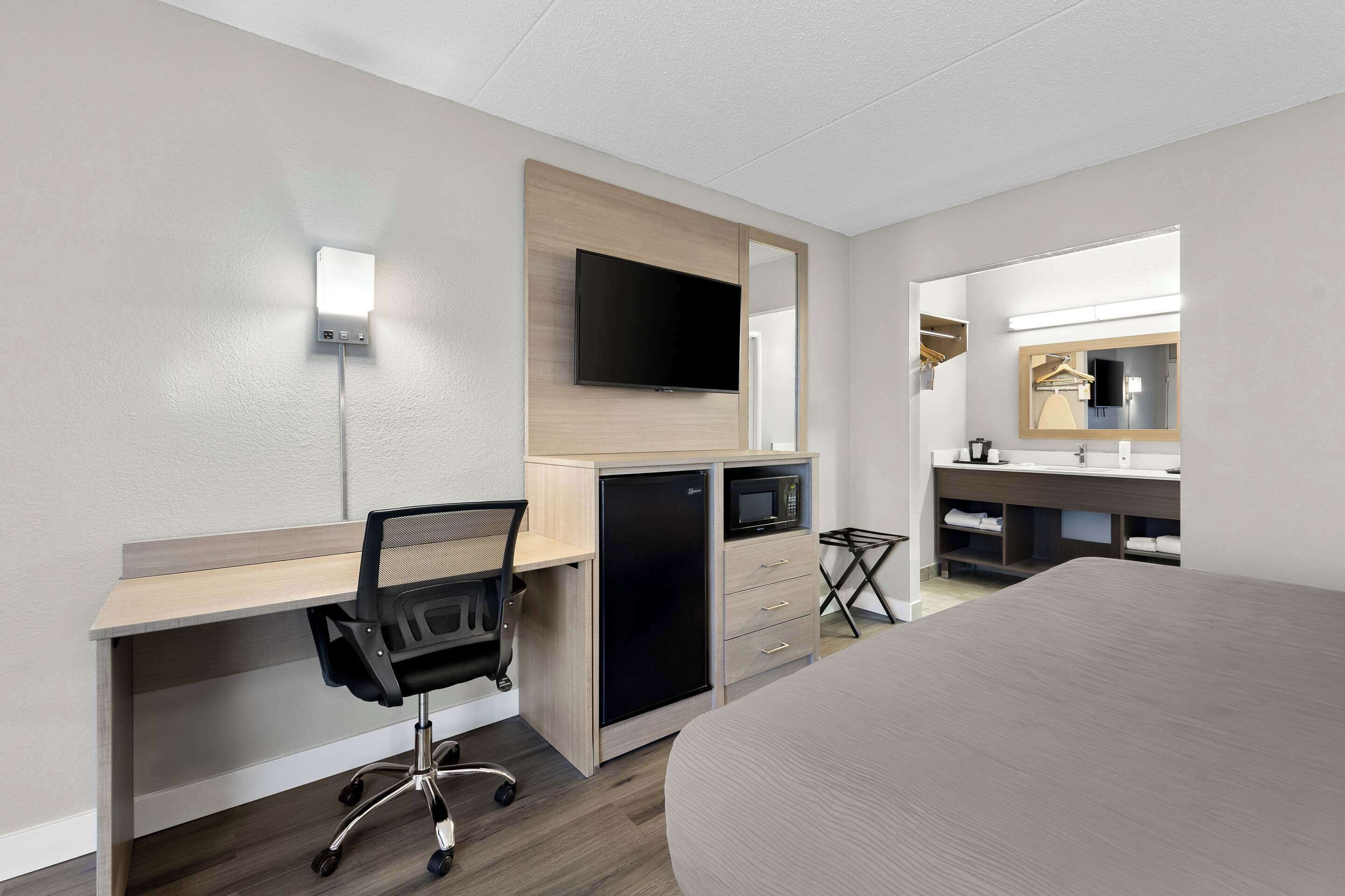 Una habitación de hotel con escritorio, silla, televisor, microondas y cama.