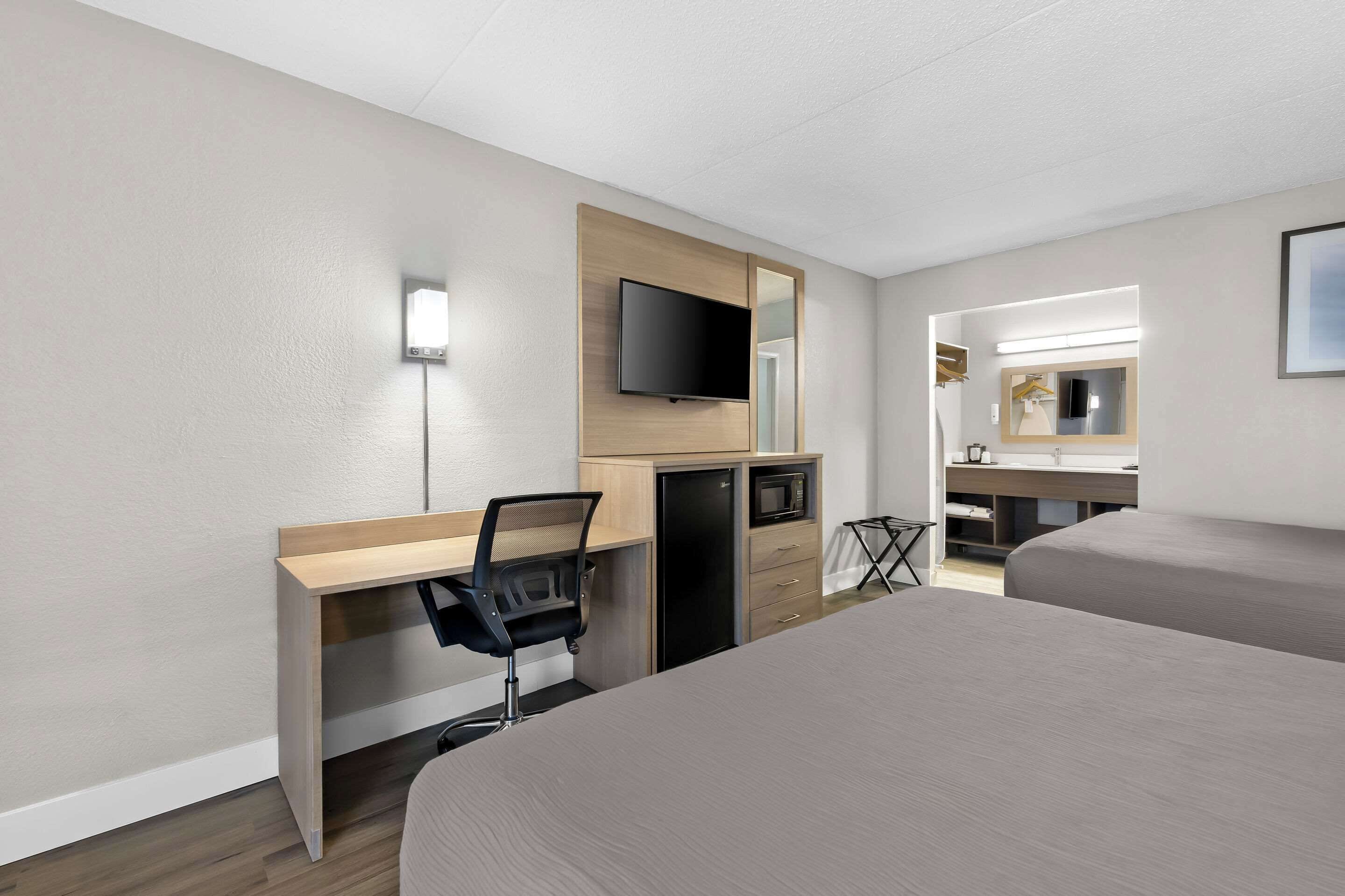 Una habitación de hotel con cama, escritorio con silla, televisor, microondas y espejo.