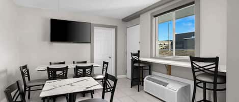 A modern dining area with a flat-screen TV, white walls, and a large window with a view.
