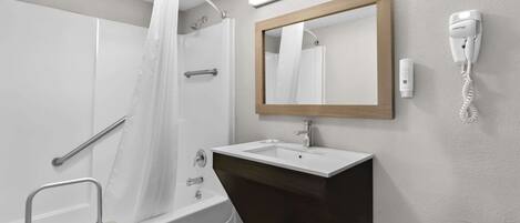 Un baño moderno con ducha, lavamanos, secador de pelo y espejo.