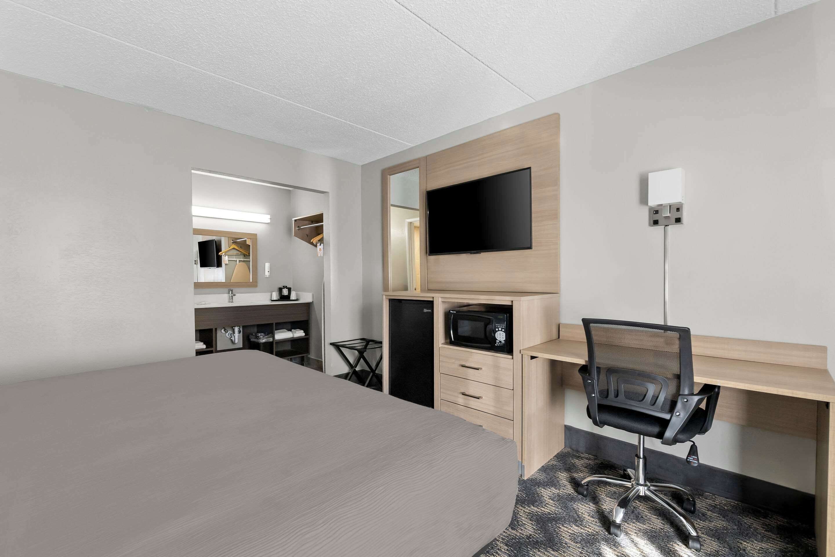 A hotel room with a large bed, a desk with a chair, a flat-screen TV, a microwave, and a small kitchenette.