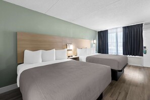 A hotel room with two beds, a wooden headboard, a nightstand with a lamp, and a window with curtains. - Quality Inn Nashville - Opryland Area (Nashville)