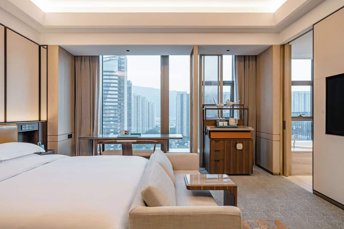 Une chambre d’hôtel moderne, dotée d’un grand lit, d’un bureau et offrant une vue sur de hauts immeubles.