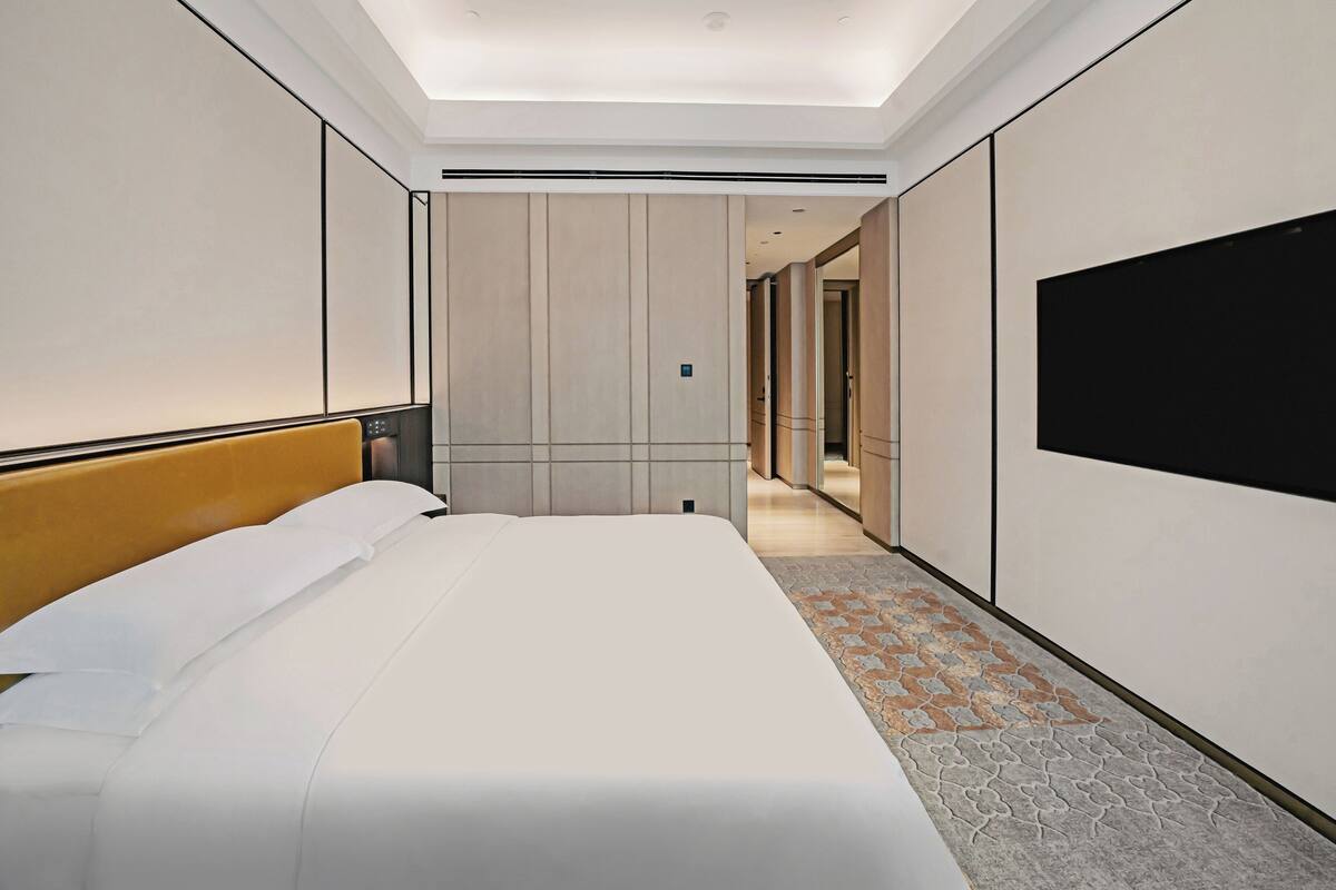 Une chambre d’hôtel avec un grand lit, un téléviseur à écran plat fixé au mur et un sol recouvert de moquette.