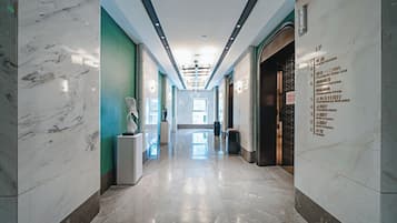 A hotel corridor with marble floors, green walls, and a clear view of the lobby in the distance.