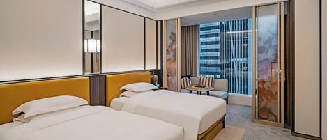 A hotel room with two beds, a sofa, a small table, and a large window with a view of a building.